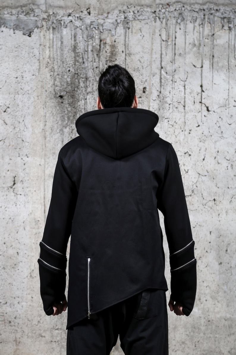 May include: A black hooded sweatshirt with zipper detailing on the sleeves and a diagonal zipper on the side. The sweatshirt has a relaxed fit and a long, asymmetrical hem.