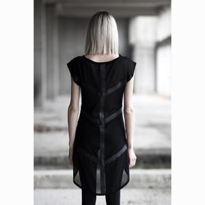 May include: Black tunic dress with short sleeves and a sheer overlay. The dress features dark, angular accents down the back. The model is facing away from the camera, showcasing the dress's design. The dress is a stylish piece of apparel.