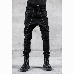 May include: Black pants with a unique design, featuring a low crotch and a tailored fit. The pants have white piping along the seams and are paired with black boots. The overall style is modern and edgy.