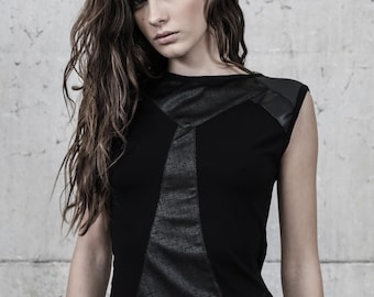 May include: A sleeveless black top featuring a central panel with a textured, dark gray fabric finish. The garment includes smooth black shoulder accents and a round neckline, constructed with a combination of solid and patterned fabric panels.