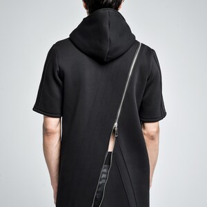 Puede incluir: Top negro con capucha y manga corta con una cremallera plateada de cuerpo entero que recorre la espalda en diagonal. El top tiene un dise&ntilde;o moderno y minimalista. El modelo lleva pantalones negros.