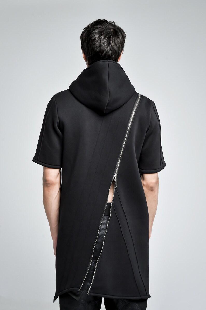 Puede incluir: Top negro con capucha y manga corta con una cremallera plateada de cuerpo entero que recorre la espalda en diagonal. El top tiene un dise&ntilde;o moderno y minimalista. El modelo lleva pantalones negros.