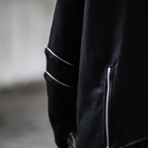 May include: Black long-sleeved shirt with a zip detail on the side and a zipped pocket on the sleeve.