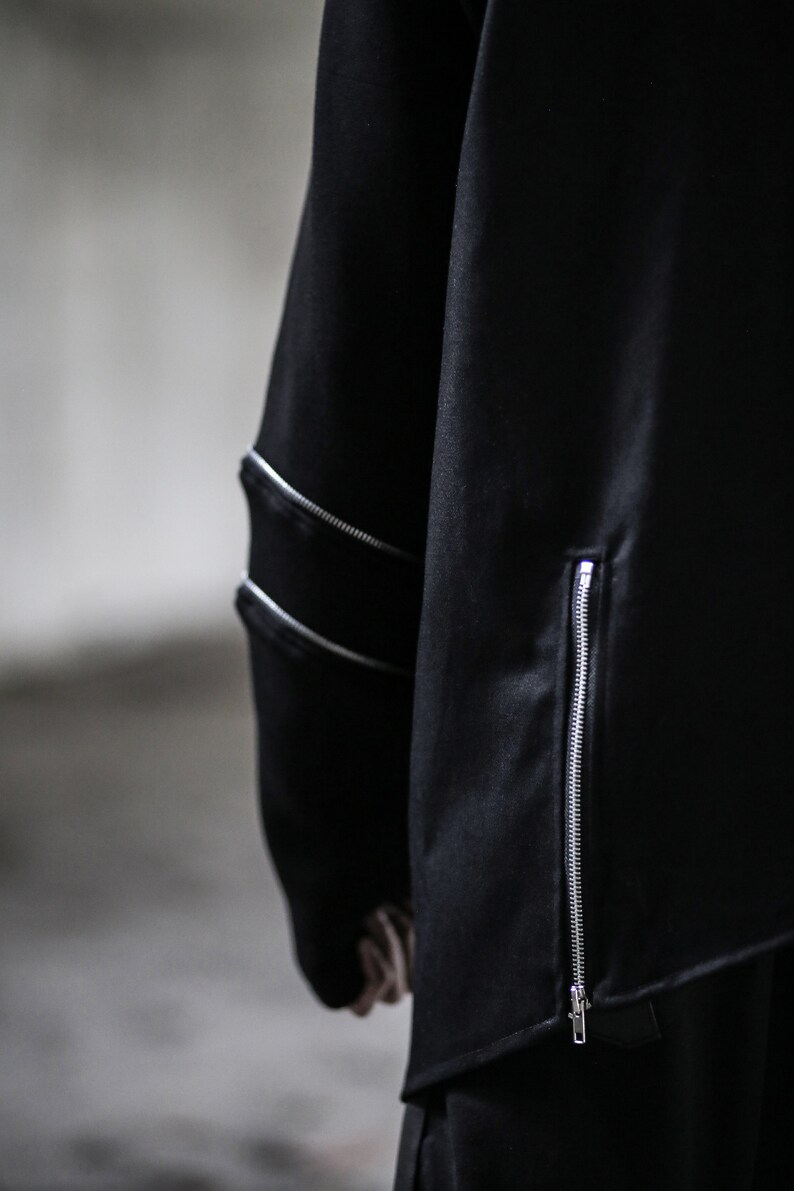 May include: Black long-sleeved shirt with a zip detail on the side and a zipped pocket on the sleeve.