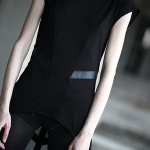 May include: Black asymmetrical top with a rectangular pocket detail and a contrasting panel. The top is paired with black mesh leggings. The overall style is minimalist and modern, with a focus on geometric shapes.