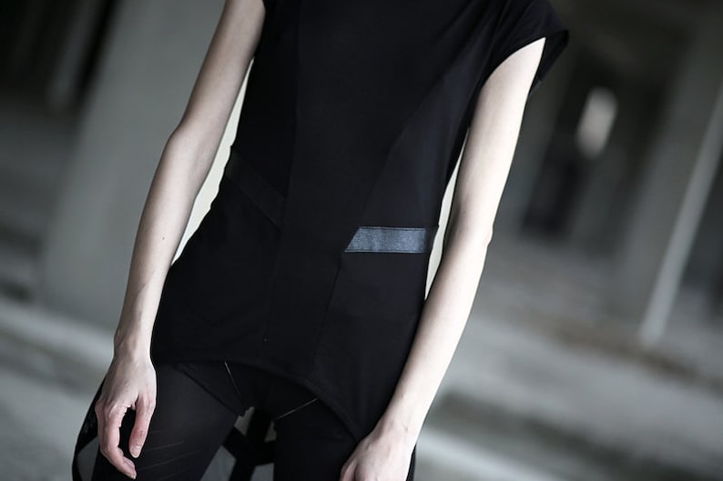 May include: Black asymmetrical top with a rectangular pocket detail and a contrasting panel. The top is paired with black mesh leggings. The overall style is minimalist and modern, with a focus on geometric shapes.