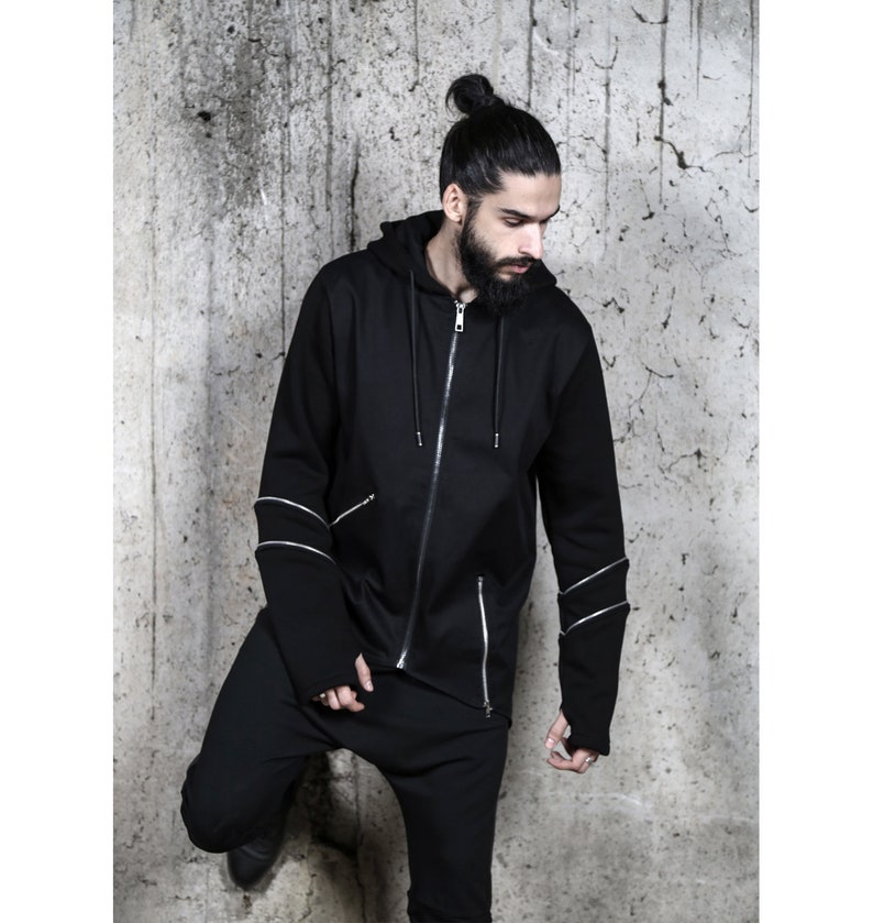 May include: Black zip-up hoodie with a long sleeve and zipper details on the sleeves. The hoodie has a hood with a drawstring.