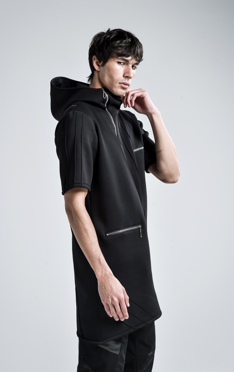 Puede incluir: Top negro con capucha y manga corta con cierre de cremallera y bolsillos laterales. El top presenta un dise&ntilde;o &uacute;nico con l&iacute;neas verticales en las mangas y una costura diagonal en la parte delantera. El modelo lleva pantalones negros.