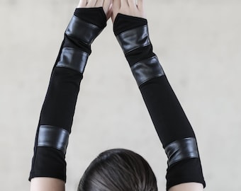May include: A pair of black fingerless gloves with leather accents. The gloves are worn by a person with their arms raised above their head.