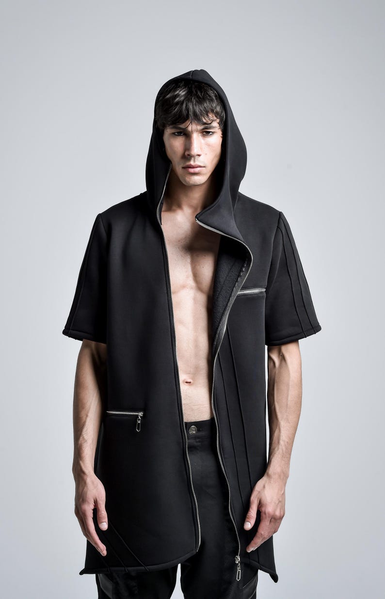 Puede incluir: Chaqueta negra con capucha y manga corta con cierre de cremallera. La chaqueta presenta un dise&ntilde;o a medida con costuras verticales y una cremallera frontal que se extiende hasta la cintura. El modelo lleva pantalones negros.