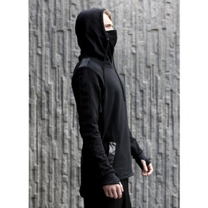 Könnte beinhalten: Ein schwarzer Kapuzenpullover mit einem langen Reißverschluss und einer schwarzen Gesichtsmaske. Der Pullover hat einen schwarzen Lederfleck an der Seite.