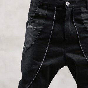 May include: Black pants with a unique design. The pants feature silver stitching along the seams and a decorative panel on the front. The fabric has a subtle sheen, and the pants have a button closure.
