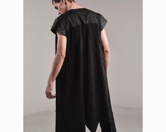 May include: A black sleeveless tunic with a unique asymmetrical hemline. The top features a textured panel across the shoulders and upper back, with vertical stitching details. The garment is part of a modern, avant-garde clothing collection.