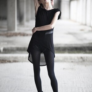 May include: A black outfit consisting of a short-sleeved top with a layered asymmetrical hem, black leggings with a geometric pattern, and black combat boots. The outfit is worn in a concrete industrial setting.
