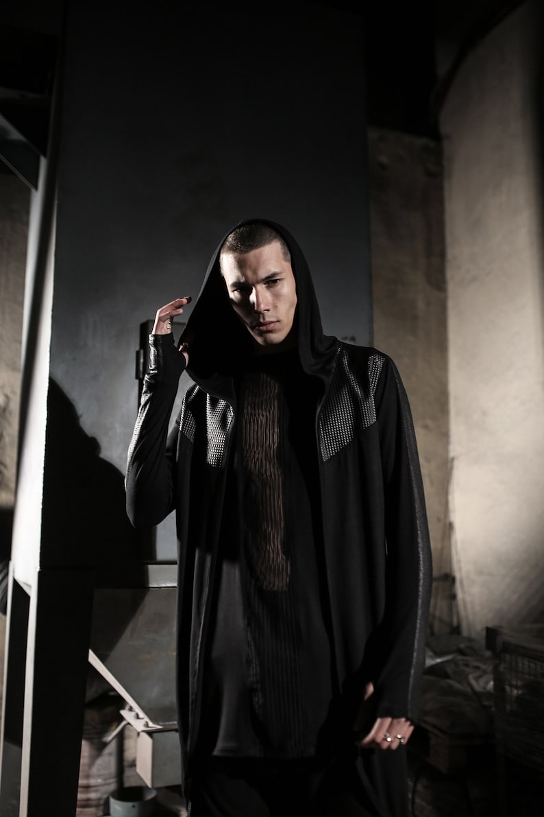May include: A black hooded long-sleeve top with a textured design on the shoulders and sleeves. The top is layered over a black shirt with a vertical striped pattern. The model is wearing a ring.