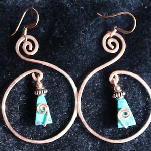 May include: A pair of copper wire earrings with turquoise gemstone drops. The earrings are shaped like a circle with a swirl at the top.