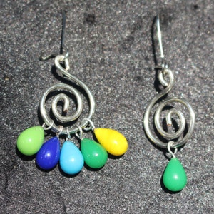 Może przedstawiać: Para srebrnych kolczyków ze spiralnym wzorem i zwisającymi, łzawiącymi koralikami szklanymi w odcieniach zieleni, błękitu i żółci.