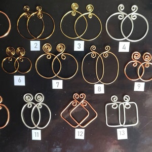 May include: A set of 13 pairs of wire earrings in various shapes and sizes. The earrings are made of copper, silver, and gold wire. The earrings are numbered 1 through 13.