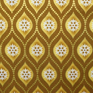 May include: A brown fabric with a repeating pattern of gold and white snowflakes. The snowflakes are inside of a teardrop shape with a gold outline. The background is a brown fabric with gold dots.