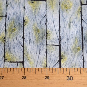 May include: Fabric with a wood plank design. The fabric features vertical planks in shades of gray and yellow, with black lines separating the planks. A wooden ruler is at the bottom, showing measurements in inches.