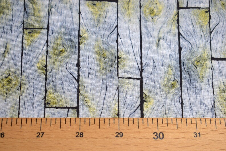 May include: Fabric with a wood plank design. The fabric features vertical planks in shades of gray and yellow, with black lines separating the planks. A wooden ruler is at the bottom, showing measurements in inches.