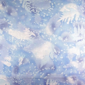May include: A fabric with a watercolor-like design in shades of blue and white. The pattern features abstract shapes, dots, and leaf-like silhouettes, creating a soft, ethereal aesthetic. The overall effect is reminiscent of a winter scene.
