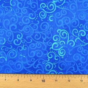 May include: Close-up of a blue fabric with a swirling, scroll-like pattern in shades of blue and teal. The fabric is measured with a wooden ruler marked in inches. This textile is suitable for various craft projects.