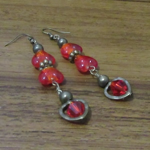 May include: A pair of dangle earrings featuring red heart-shaped glass beads and metal accents.