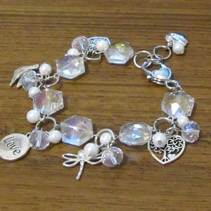 May include: A silver charm bracelet featuring clear crystal beads, white pearl beads, and a variety of silver charms, including a dragonfly, a heart with a tree, a heart with a wing, and a charm inscribed with the word "Love".