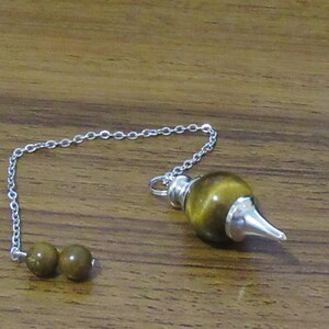 May include: A silver chain with a brown and gold tiger's eye pendulum with a pointed tip. The chain has two brown beads at the end.