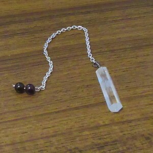 May include: A clear crystal pendulum with a silver chain and two black beads at the top.