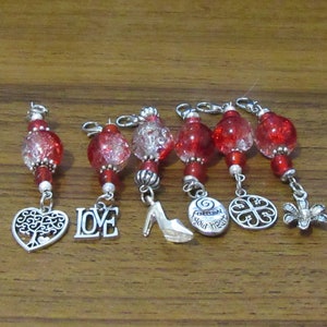 May include: Seven red glass bead charms with silver accents and different charms attached. The charms include a tree in a heart, the word "LOVE", a high heel shoe, a circle with the text "Follow your heart", a four-leaf clover, and a flower.