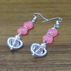 Puede incluir: Un par de pendientes colgantes de plata con cuentas de cristal rosa y detalles de cristal.