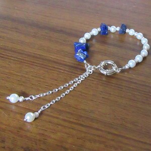 May include: A white pearl and blue lapis lazuli bracelet with a silver chain and clasp. The bracelet has a dangling pearl charm.