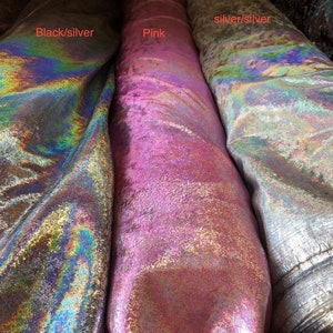May include: Close-up of three rolls of fabric in iridescent colours. The fabric on the left is black and silver, the middle is pink, and the right is silver and silver. The fabric has a shiny, textured surface.