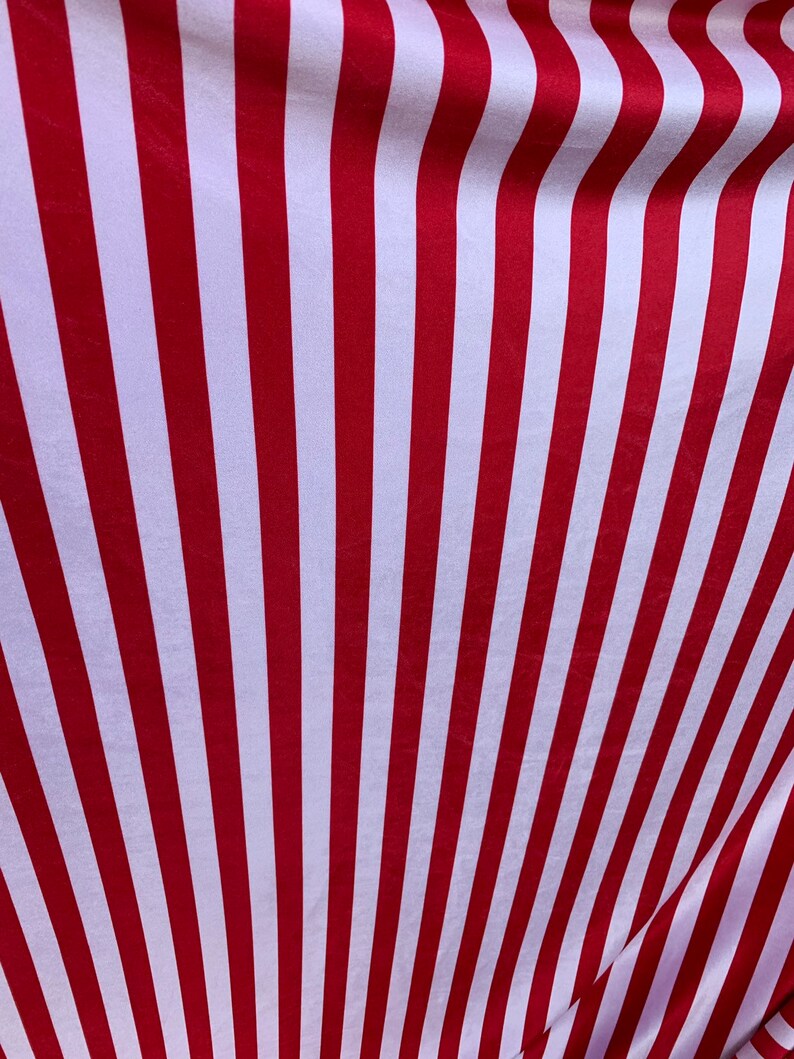 May include: Red and white striped fabric with a subtle sheen. The fabric is folded and draped, creating a wavy pattern.