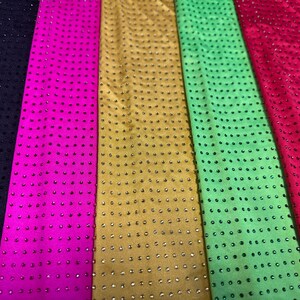 Op de afbeelding: Zes verticale stroken stof in donkerpaars, felroze, goud, lichtgroen, rood en talingblauw. Elke strook heeft een uniform rasterpatroon van kleine, reflecterende, ronde studs of strass-steentjes in consistente verticale en horizontale rijen.