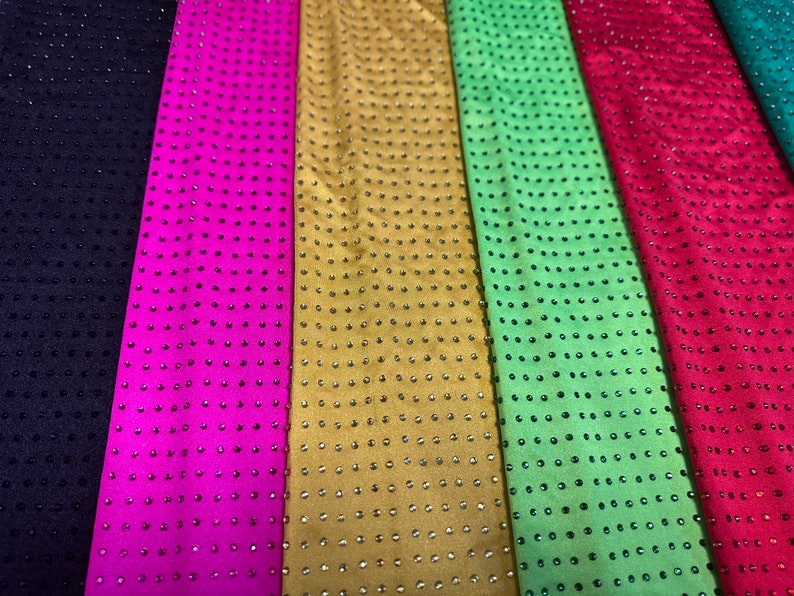Op de afbeelding: Zes verticale stroken stof in donkerpaars, felroze, goud, lichtgroen, rood en talingblauw. Elke strook heeft een uniform rasterpatroon van kleine, reflecterende, ronde studs of strass-steentjes in consistente verticale en horizontale rijen.