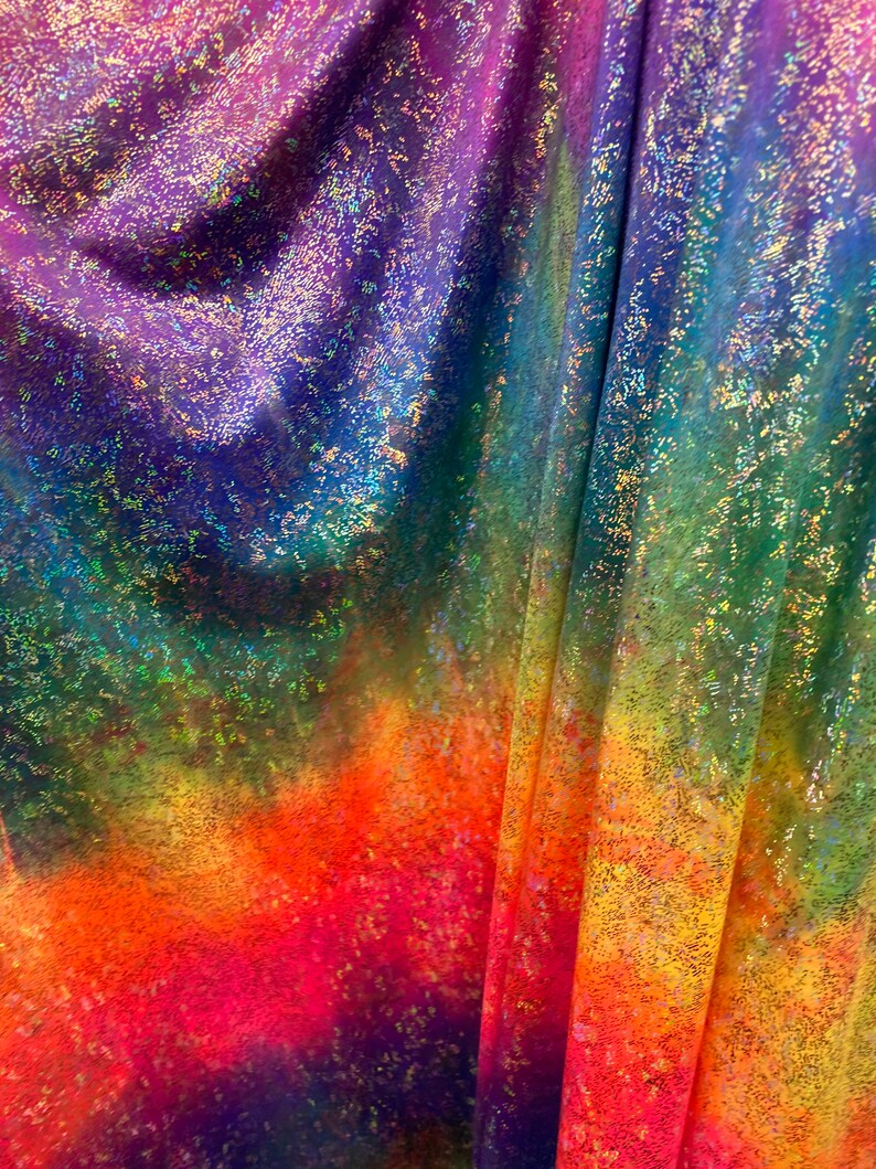 K&ouml;nnte beinhalten: Ein regenbogenfarbener, schimmernder Stoff mit einer gesprenkelten Textur. Der Stoff ist gefaltet und zeigt einen Farbverlauf von Lila bis Gelb.