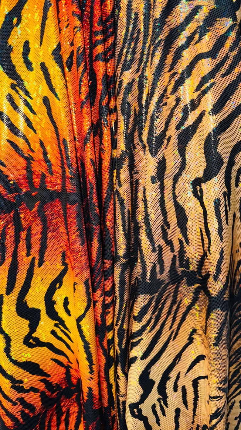 Puede incluir: Primer plano de una tela con un patr&oacute;n de rayas de tigre en naranja, negro y amarillo. La tela tiene un acabado brillante e iridiscente.