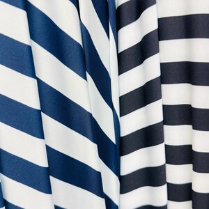 K&ouml;nnte beinhalten: Nahaufnahme von drei Stoffen mit kr&auml;ftigen, horizontalen Streifen. Die Stoffe weisen marineblaue und wei&szlig;e Streifen sowie schwarz-wei&szlig;e Streifen auf. Der Stoff ist drapiert und erzeugt weiche Falten und Schatten.