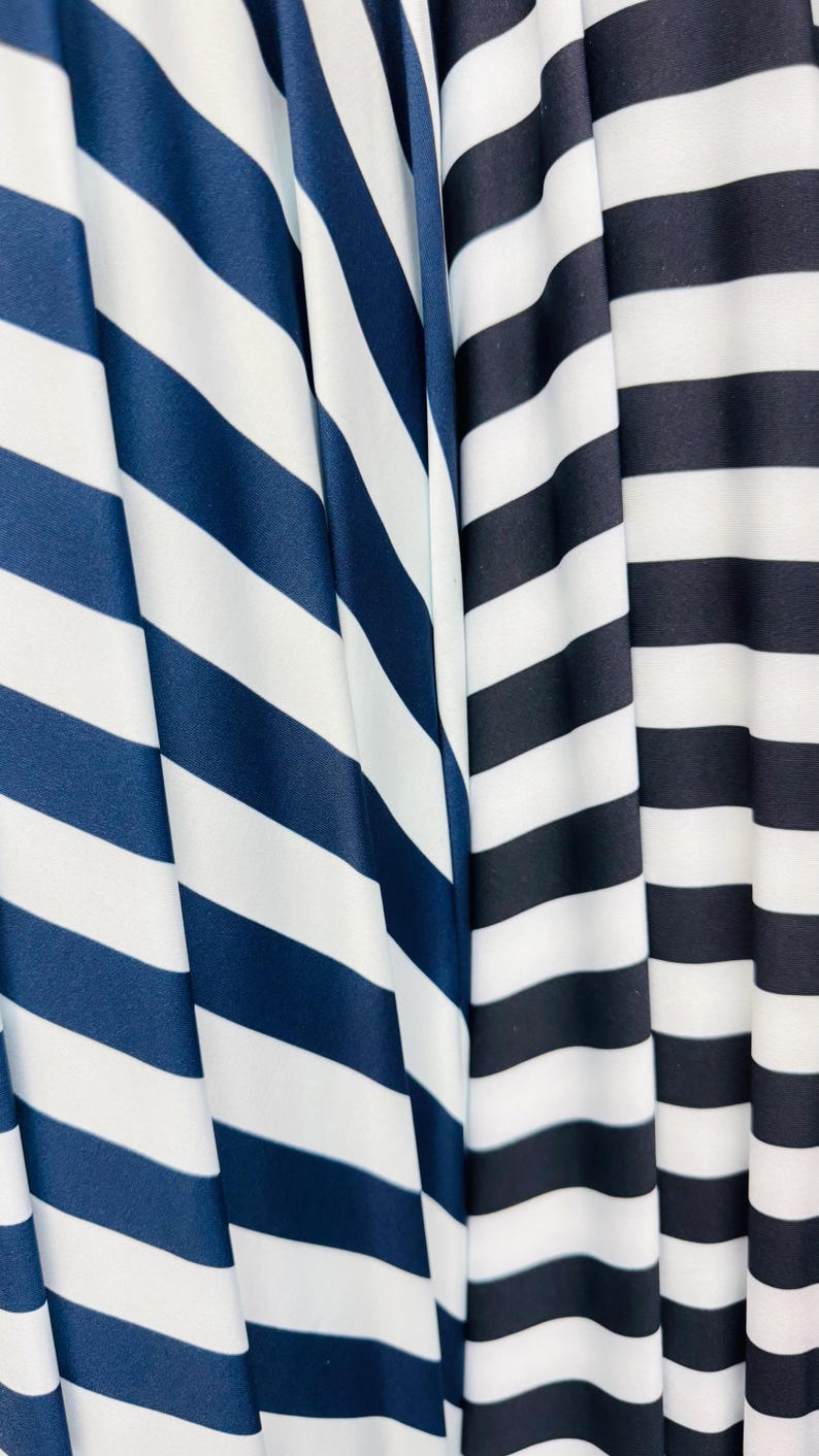 K&ouml;nnte beinhalten: Nahaufnahme von drei Stoffen mit kr&auml;ftigen, horizontalen Streifen. Die Stoffe weisen marineblaue und wei&szlig;e Streifen sowie schwarz-wei&szlig;e Streifen auf. Der Stoff ist drapiert und erzeugt weiche Falten und Schatten.
