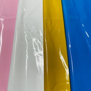 Könnte beinhalten: Nahaufnahme von vier Stoffproben in Pink, Weiß, Gelb und Blau. Der Stoff hat eine glänzende, glatte Oberfläche.