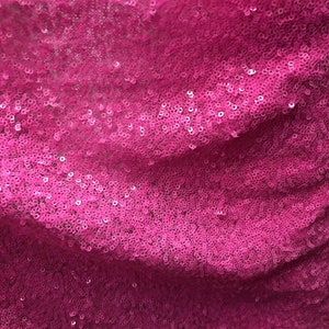 May include: Pink sequined fabric with a subtle shimmer. The sequins are closely packed together, creating a smooth and luxurious texture.