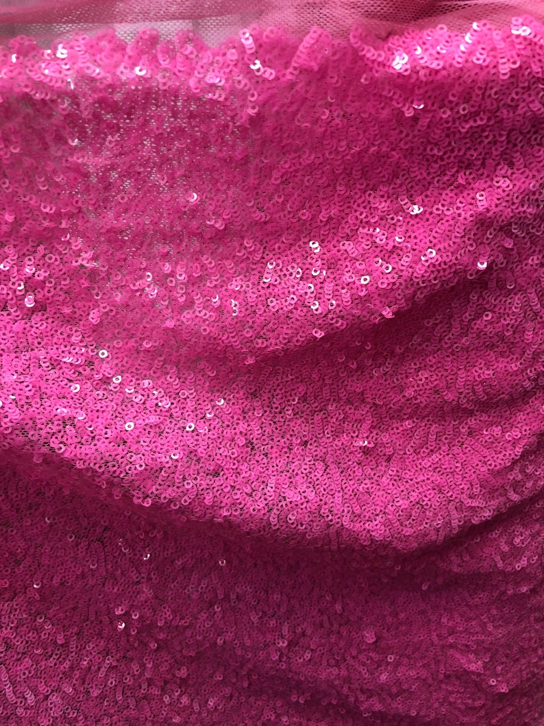 May include: Pink sequined fabric with a subtle shimmer. The sequins are closely packed together, creating a smooth and luxurious texture.