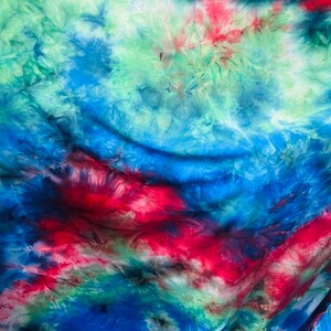 May include: A vibrant tie-dye fabric with a swirling pattern of red, blue, and green hues. The colors blend and bleed into each other, creating a dynamic and textured effect. The fabric appears soft and flowing.