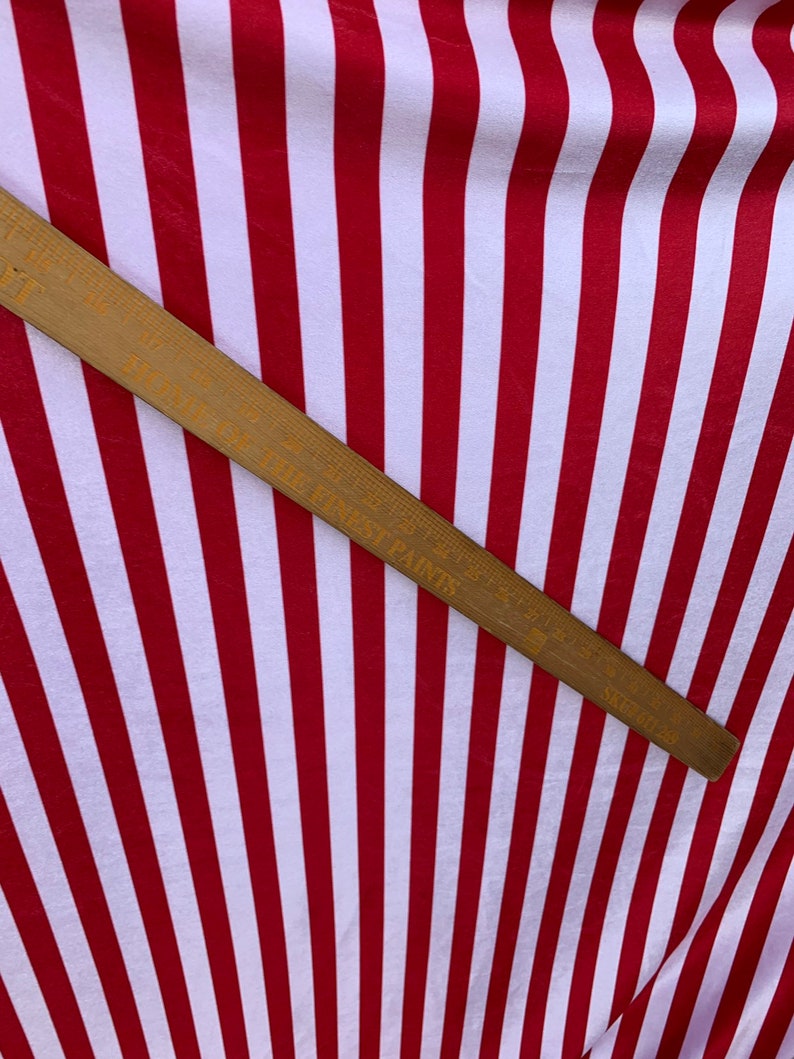May include: Red and white striped fabric with a wooden ruler measuring 36 inches. The ruler has the words "Made in West Paris" printed on it.
