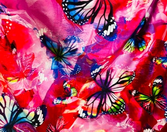 May include: A pink fabric with a colorful butterfly print. The butterflies are in various shades of blue, green, yellow, and pink. The fabric has a soft, silky texture.