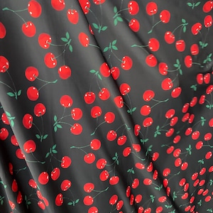 May include: Black fabric with a repeating pattern of red cherries with green stems and leaves.