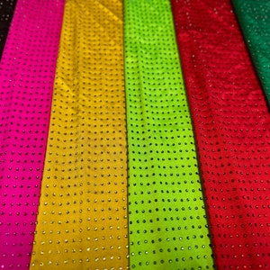 Op de afbeelding: Een collectie verticale stroken stof in zwart, felroze, goud, limoengroen, rood, smaragdgroen en wit. Elke strook is voorzien van een uniform raster van kleine, reflecterende, ronde studs of strass-steentjes in consistente rijen en kolommen.